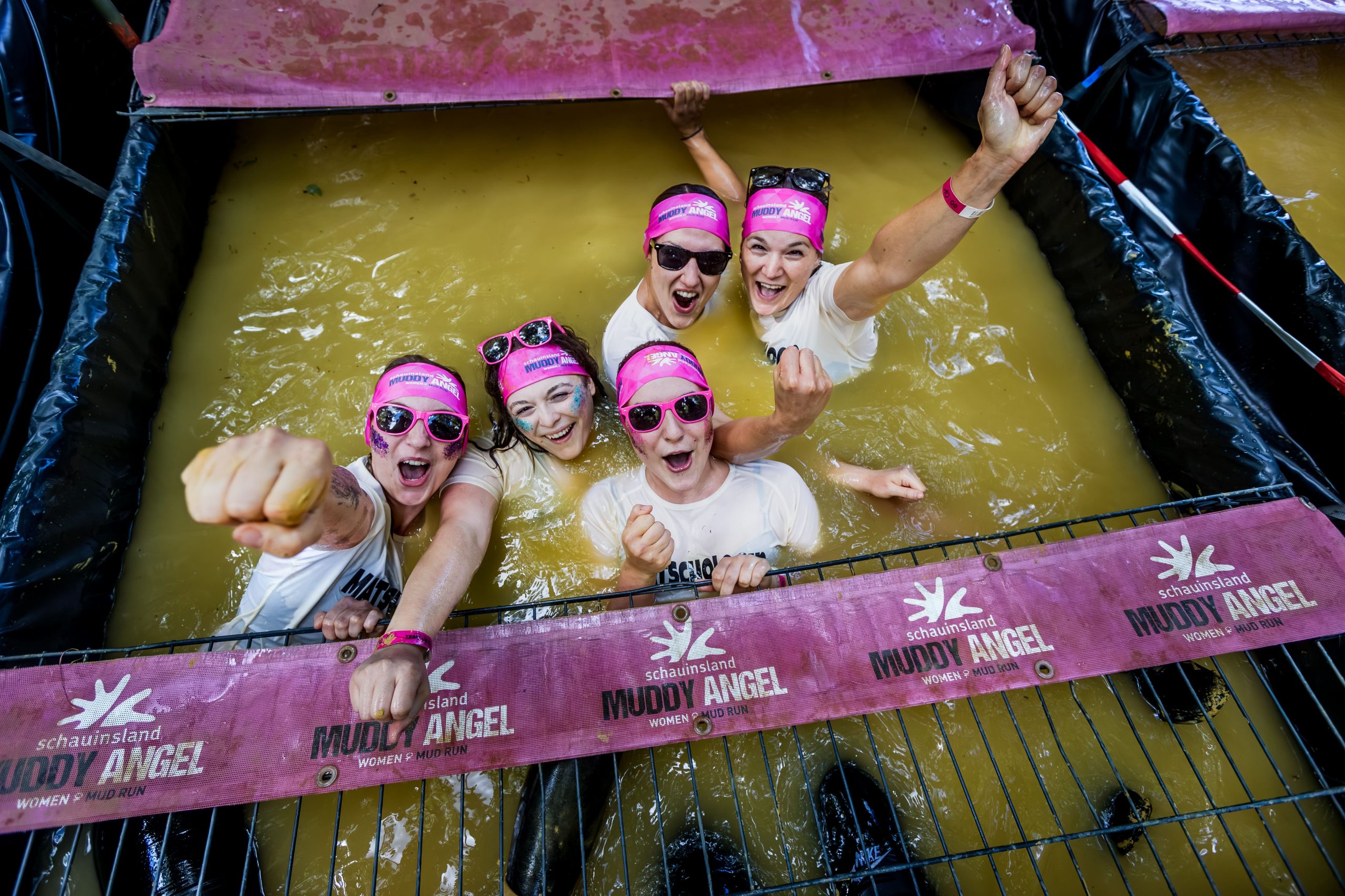 Fünf Teilnehmerinnen jubeln gemeinsam in einem Wasserhindernis des schauinsland Muddy Angel Runs.