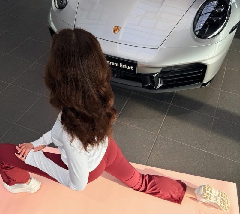 Teilnehmerin macht Dehnübung auf Yogamatte vor Porsche Sportwagen im Showroom Erfurt