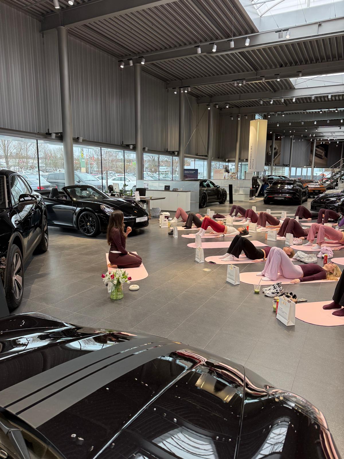 Yoga-Gruppe auf Matten im Porsche Showroom zwischen Sportwagen während eines Events